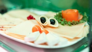 A plate with various food items, including a rolled omelette, a slice of cheese, and some vegetables. - Hotel Astoria (Karlsruhe)