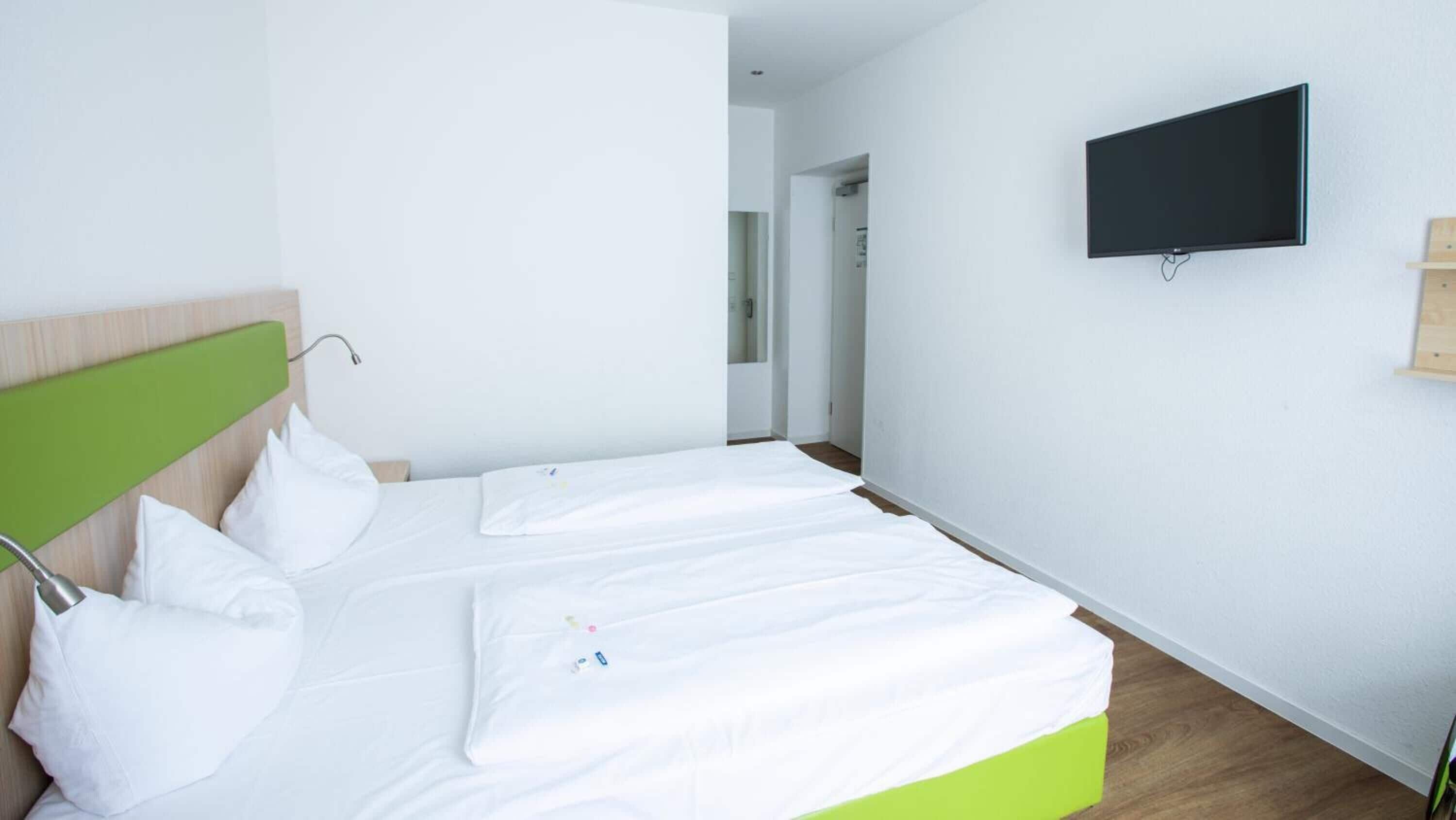 A hotel room with two single beds, a flat-screen TV mounted on the wall, and a wooden floor.