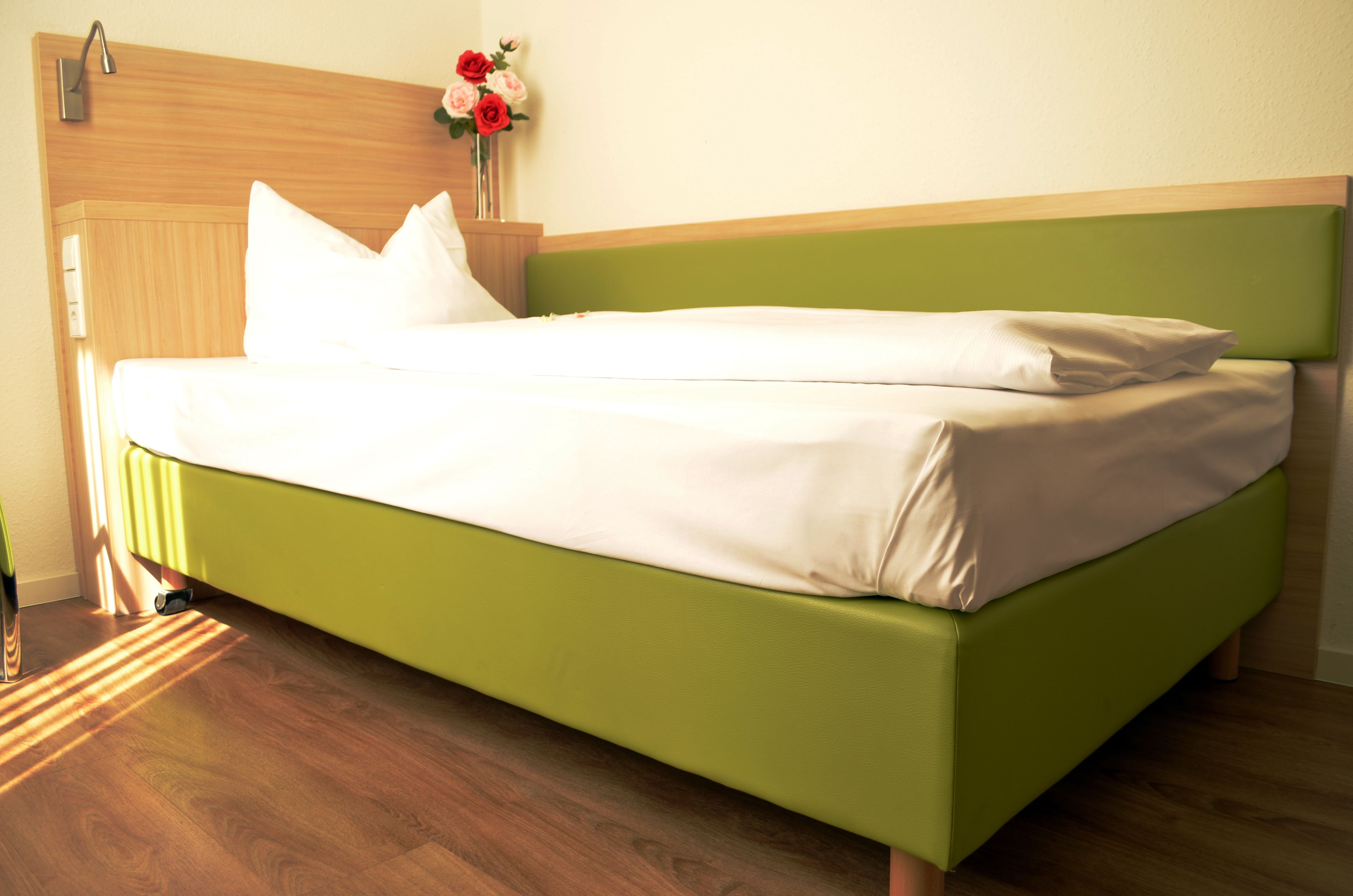A neatly made bed with a green headboard and white bedding in a room with wooden flooring and a wooden headboard.
