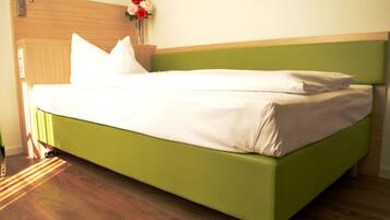 A neatly made bed with a green headboard and white bedding in a room with wooden flooring and a wooden headboard.