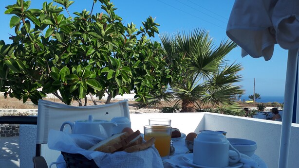 A table set with breakfast items, including bread, eggs, and juice, overlooking a scenic view with palm trees and the sea. - Paradisos Oia (Santorini)