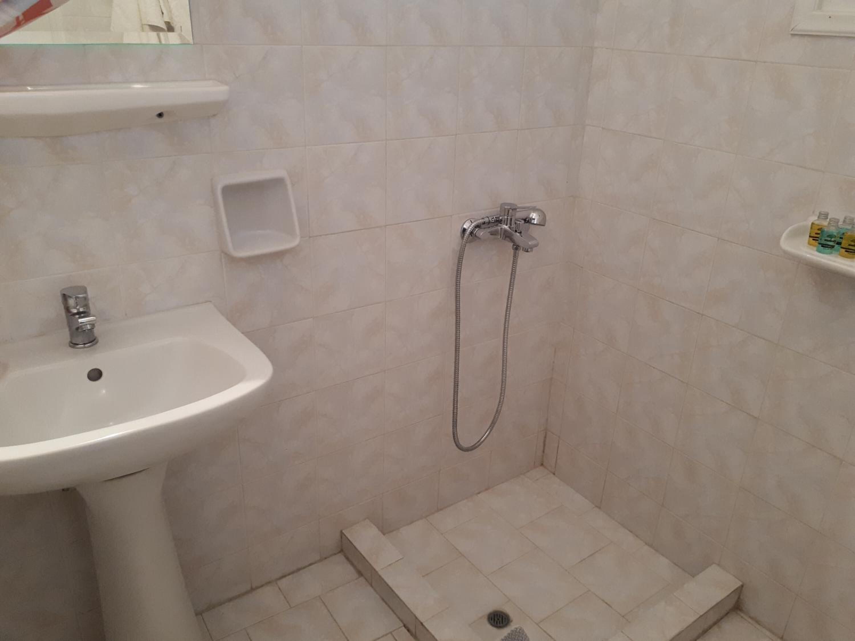 Un baño con lavamanos, ducha y un estante pequeño con artículos de aseo.