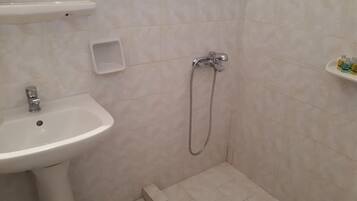 Un baño con lavamanos, ducha y un estante pequeño con artículos de aseo.