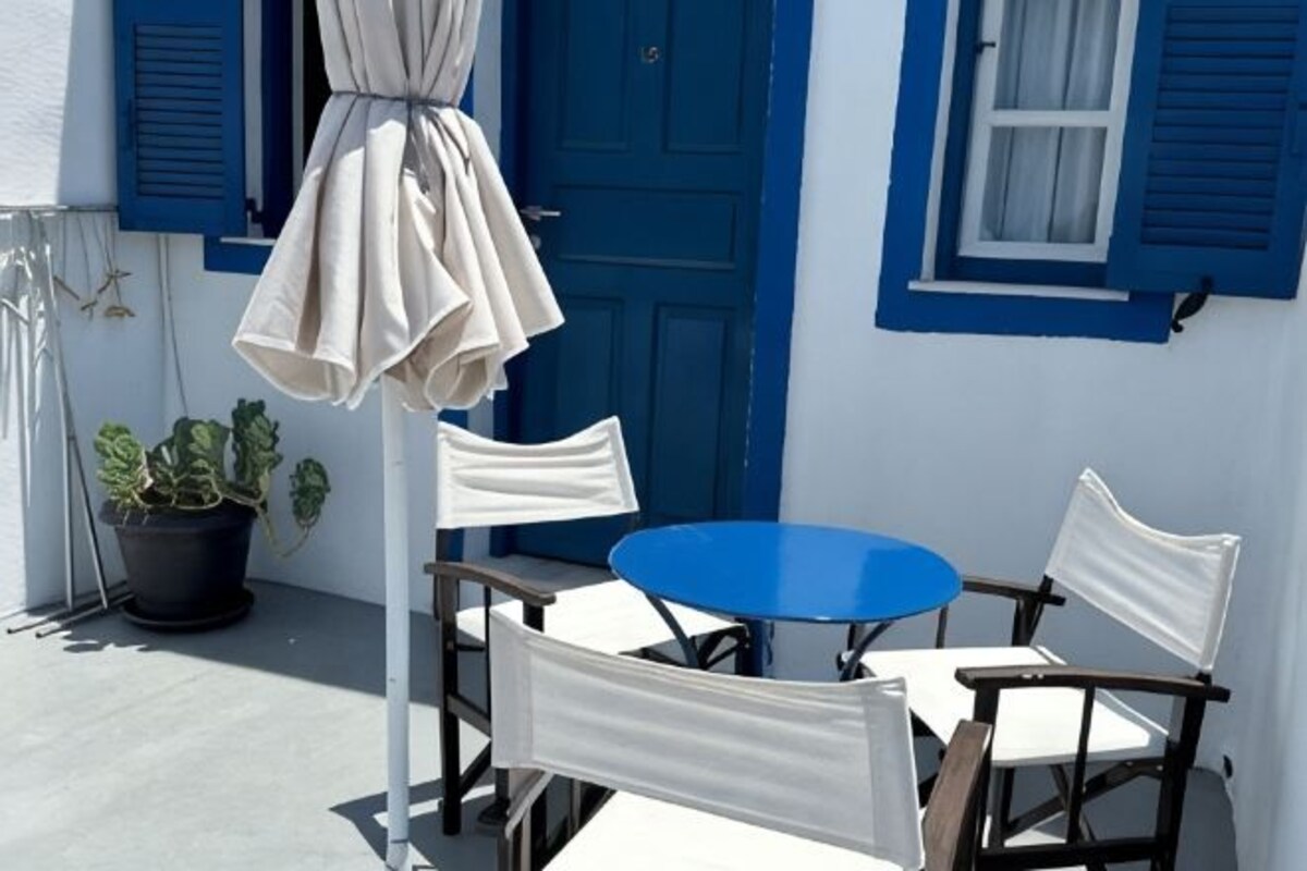 Un petit espace extérieur aménagé avec une table ronde et quatre chaises, une plante en pot et une porte bleue.