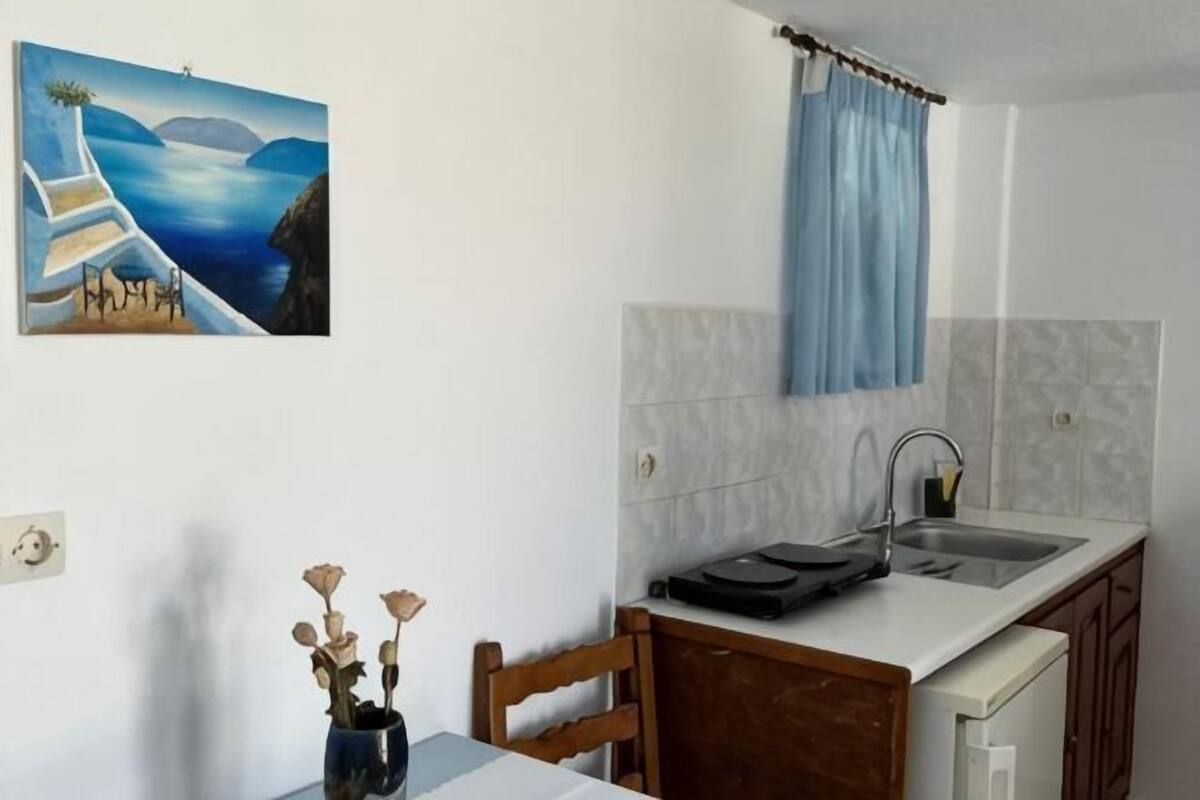 A kitchen with a sink, a blue curtain, a painting, and a vase with dried flowers.