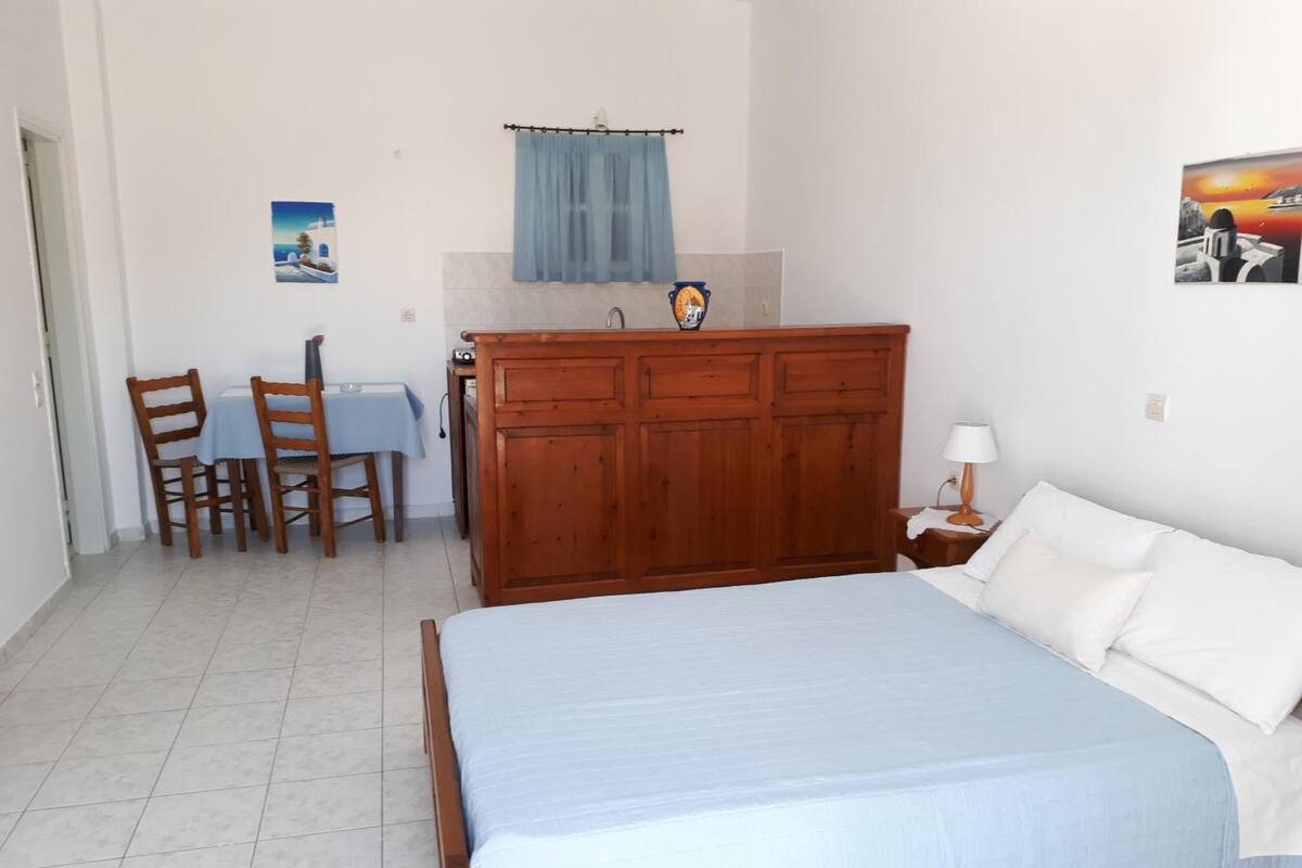 A bedroom with a bed, a wooden dresser, a desk with chairs, and a bathroom with a towel hanging.