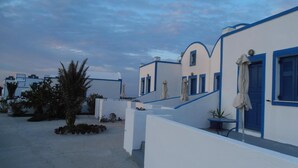 A row of white buildings with blue accents, likely part of a hotel or resort. - Paradisos Oia (Santorini)