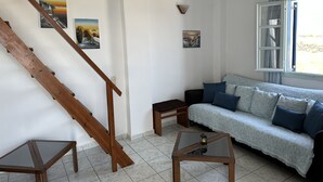 A living room with a wooden staircase, a sofa with blue cushions, a small table with a lantern, and two wall-mounted pictures. - Paradisos Oia (Santorini)