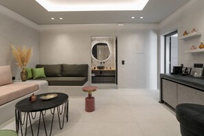 A modern living room with a sofa, a round coffee table, and a dining area with a small table and chairs. - Iphimedeia Apartments & Suites (Naxos)