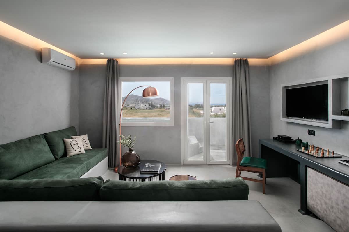 A modern living room with a green sofa, a coffee table, a TV mounted on the wall, and a view of a building through the window.