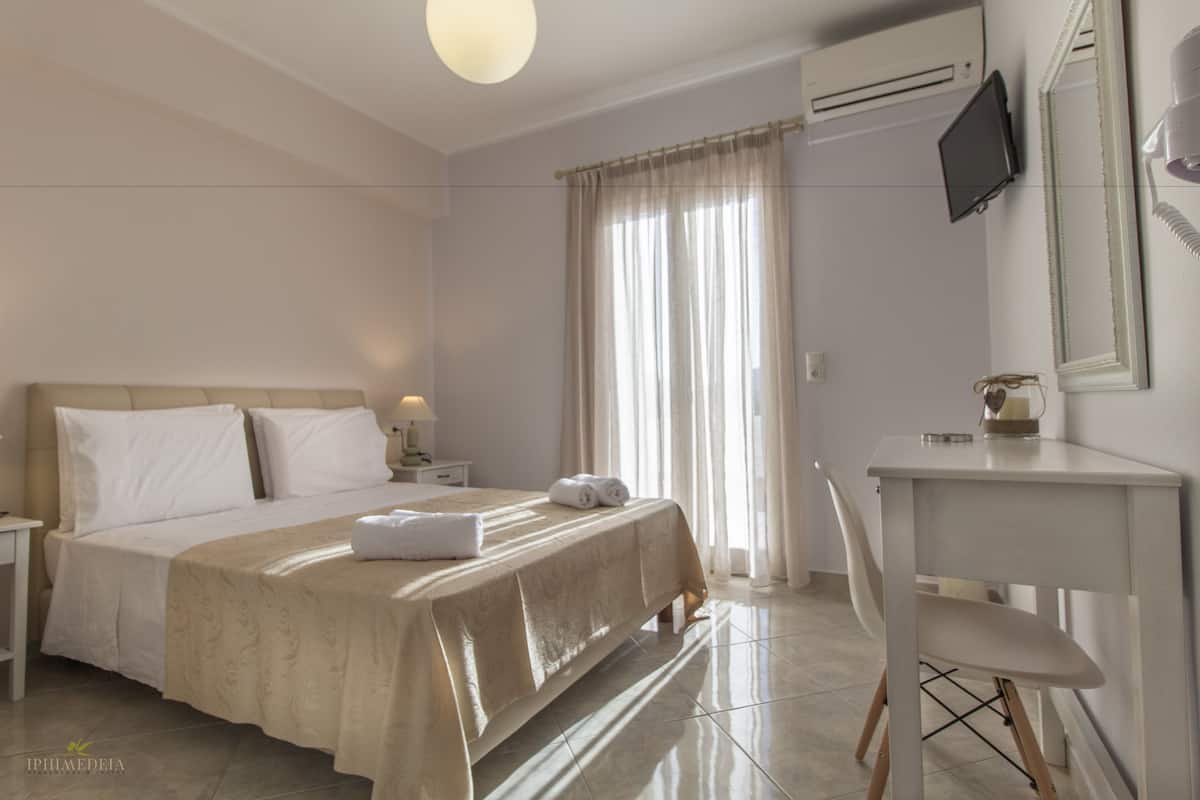 A hotel room with a bed, a desk, a chair, a TV, and a window with curtains.