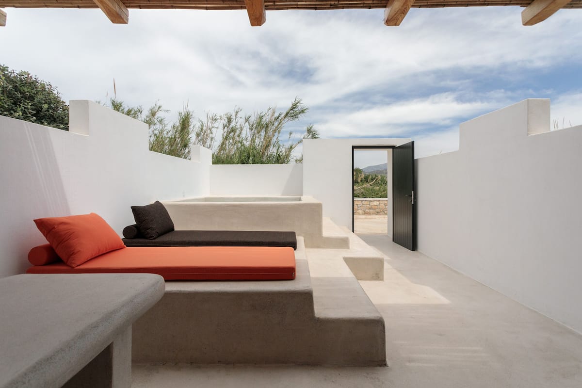 A modern outdoor seating area with a concrete bench and cushions, a clear view of the surrounding landscape, and a door leading to another space.