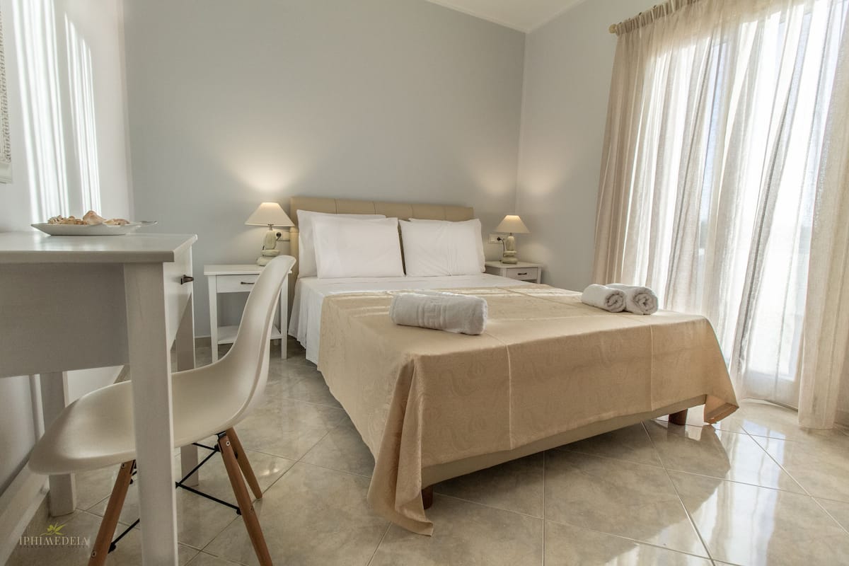 A hotel room with a bed, two bedside tables with lamps, a chair, a desk, and a window with curtains.