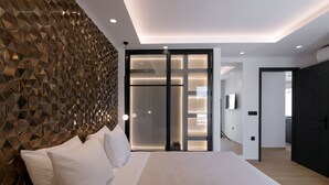Un dormitorio moderno con un cabecero de diseño geométrico, una cama grande con ropa blanca y un puerta corrediza de vidrio que da al baño.