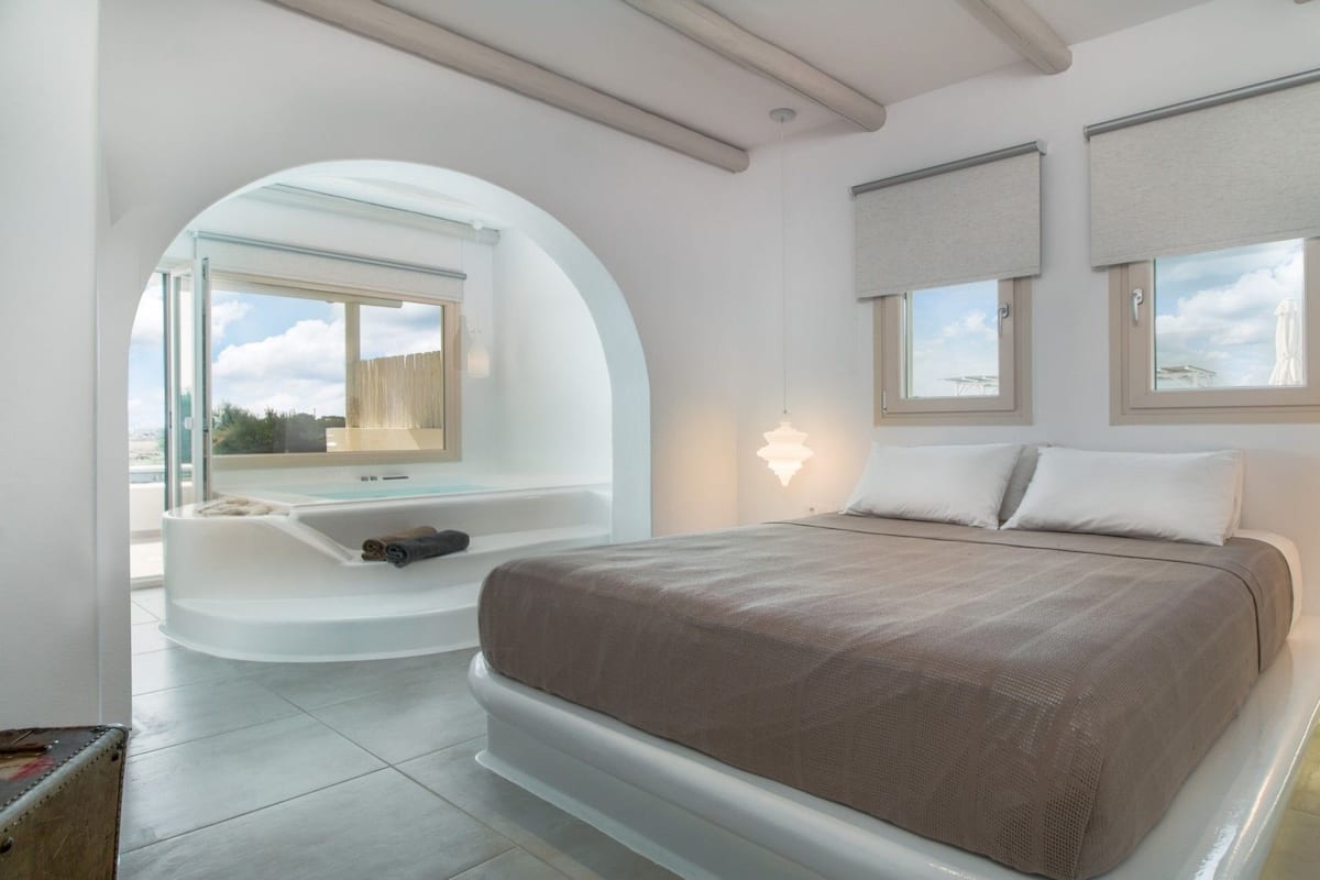 A modern bedroom with a large bed, a built-in bathtub, and a view of the city.