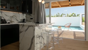 Una cocina moderna con encimeras de mármol, una zona de bar con taburetes y vistas a una piscina.