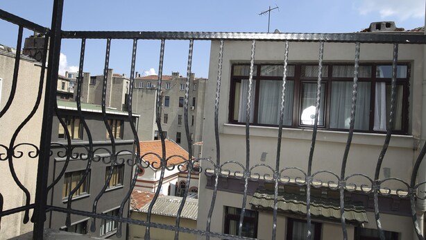 Un balcon doté d’une balustrade en métal, d’un sol carrelé et offrant une vue sur les bâtiments en arrière-plan.