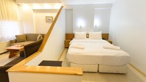 Une chambre d’hôtel avec un canapé, un lit avec du linge de lit blanc, une table de chevet en bois et une petite table.