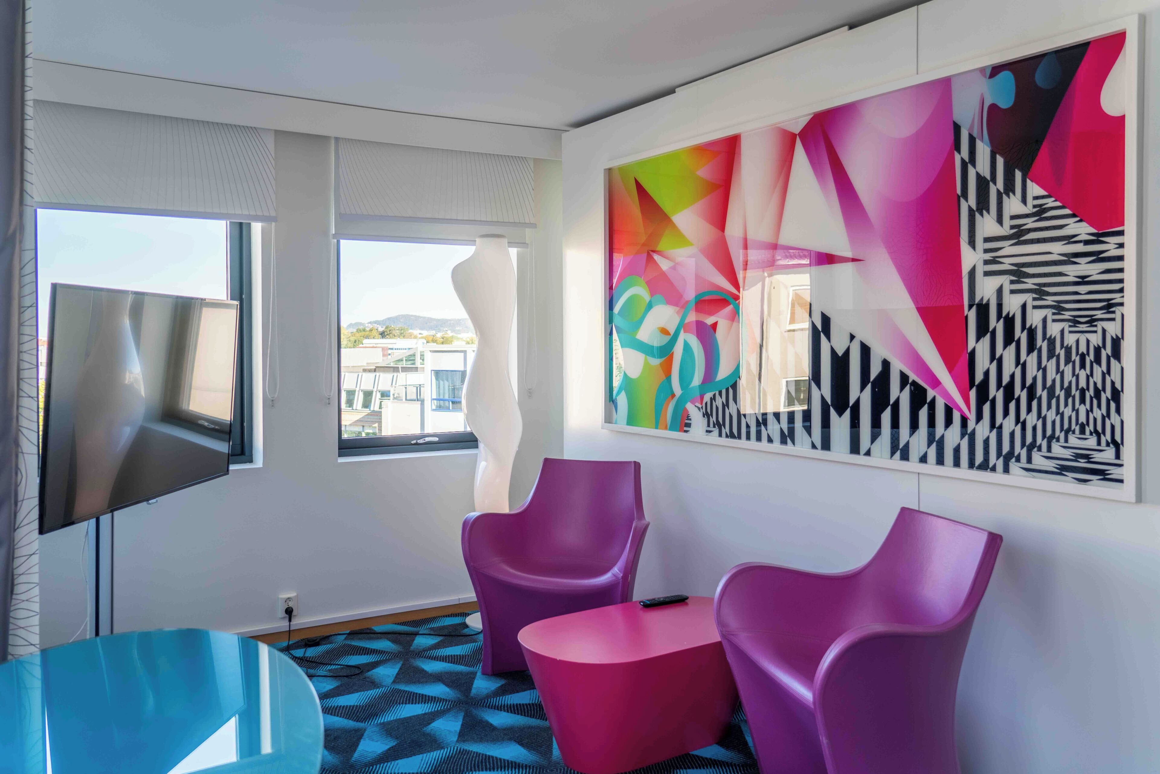 Une chambre moderne avec un grand tableau abstrait, un téléviseur à écran plat et des fauteuils violets.