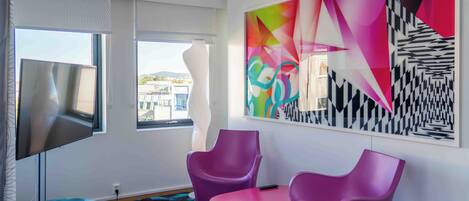 Une chambre moderne avec un grand tableau abstrait, un téléviseur à écran plat et des fauteuils violets.