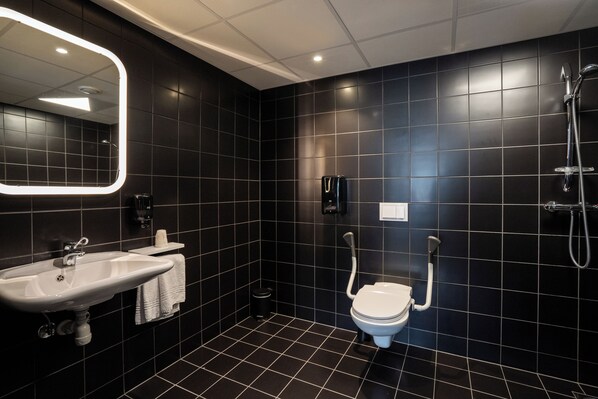 Un baño moderno con piso de baldosas negras, un lavamanos blanco, un inodoro y una ducha.