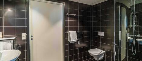 Un baño moderno con un inodoro blanco, ducha con mampara de vidrio y lavamanos con toallero.