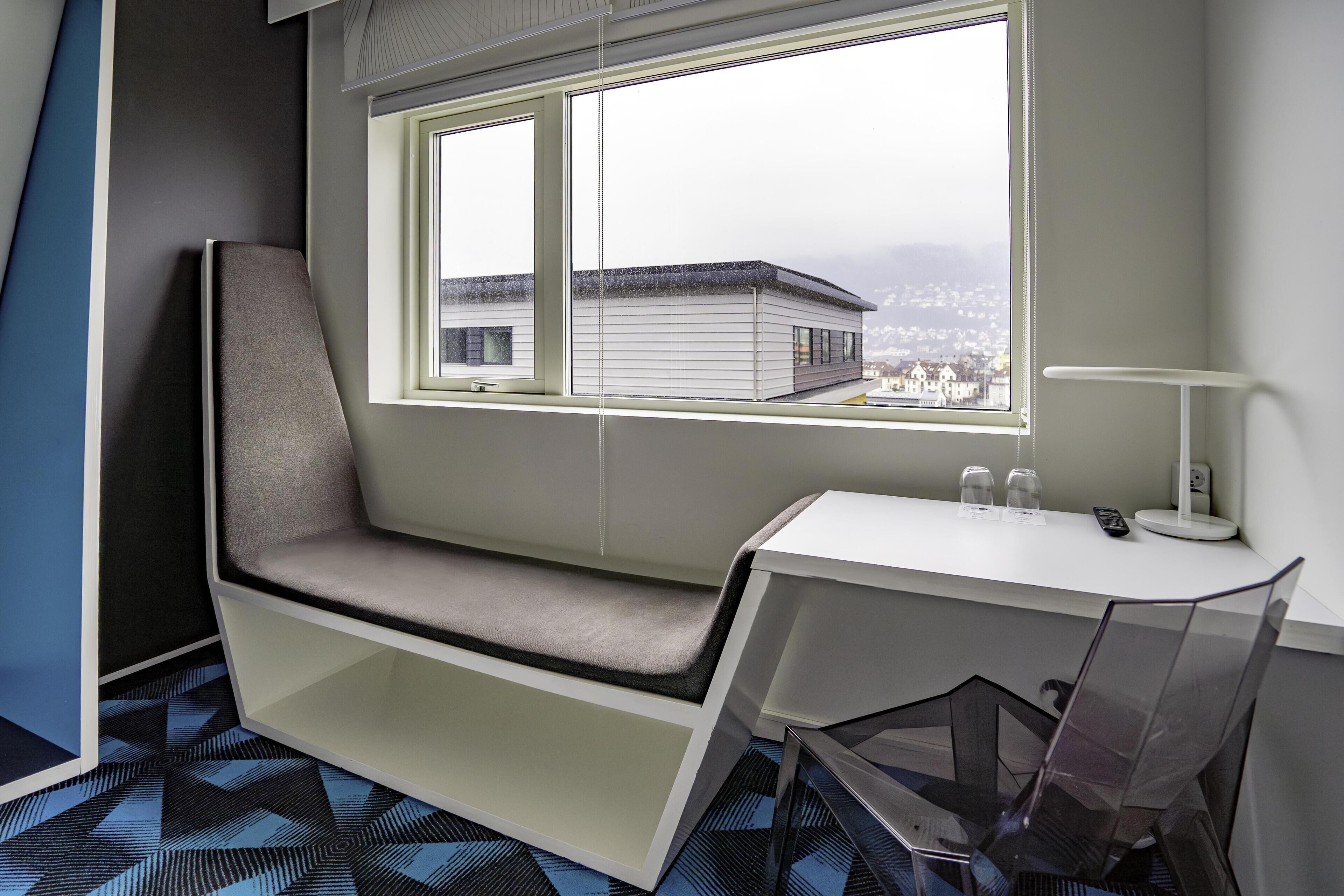 Una habitación de hotel moderna con un banco incorporado junto a la ventana, un escritorio y una silla.