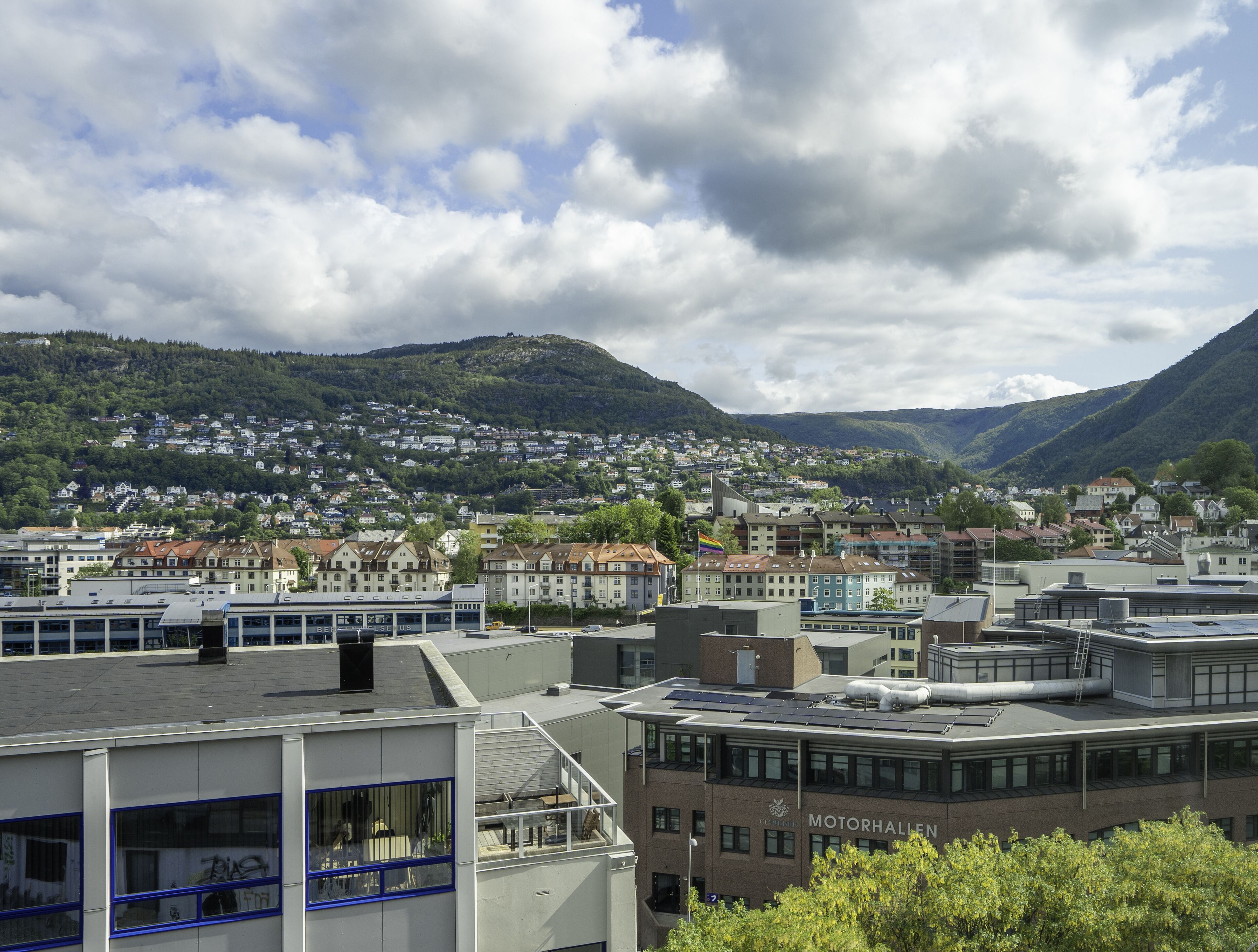 A cityscape with a prominent building labeled "MOTORHALLEN" featuring a modern design with large windows and solar panels.