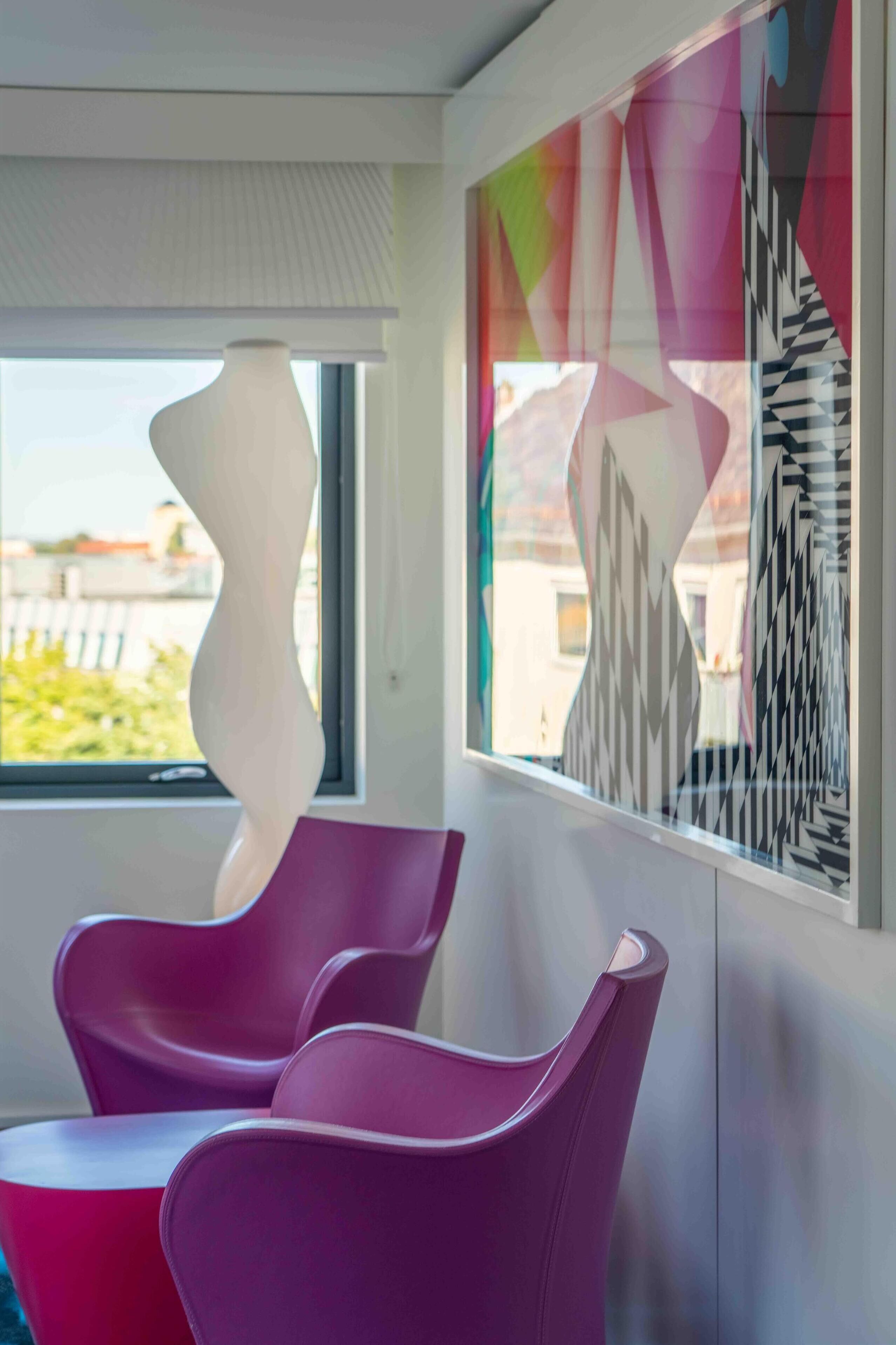 A modern interior with two purple chairs, a white abstract sculpture, and a colorful geometric wall art piece.
