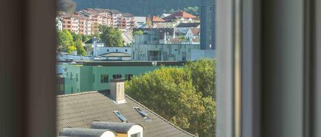 A view through a window of a building with multiple balconies, a mountain in the background, and a distant tower.