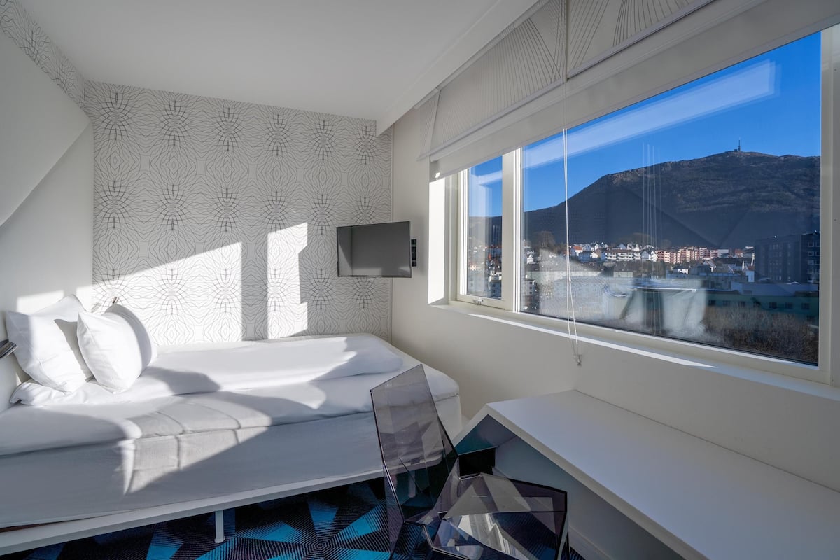 A modern bedroom with a bed, a TV, and a large window with a city view.