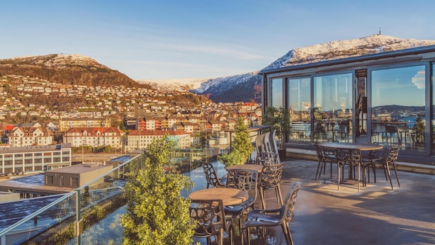 A rooftop terrace with outdoor seating, a glass wall offering a city view, and a snow-capped mountain in the background. - Prize by Radisson, Solheimsviken Bergen (Bergen)