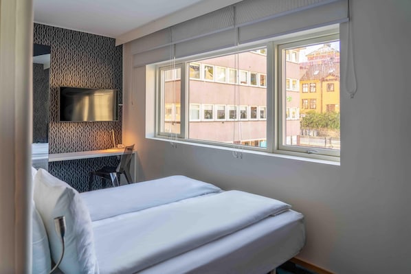 Habitación de hotel con cama, televisor montado en la pared y ventana con vistas a edificios.