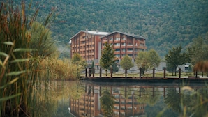 A multi-story building with a modern architectural design, situated by a calm body of water with reflections. - Chenot Palace Gabala (Gabala)