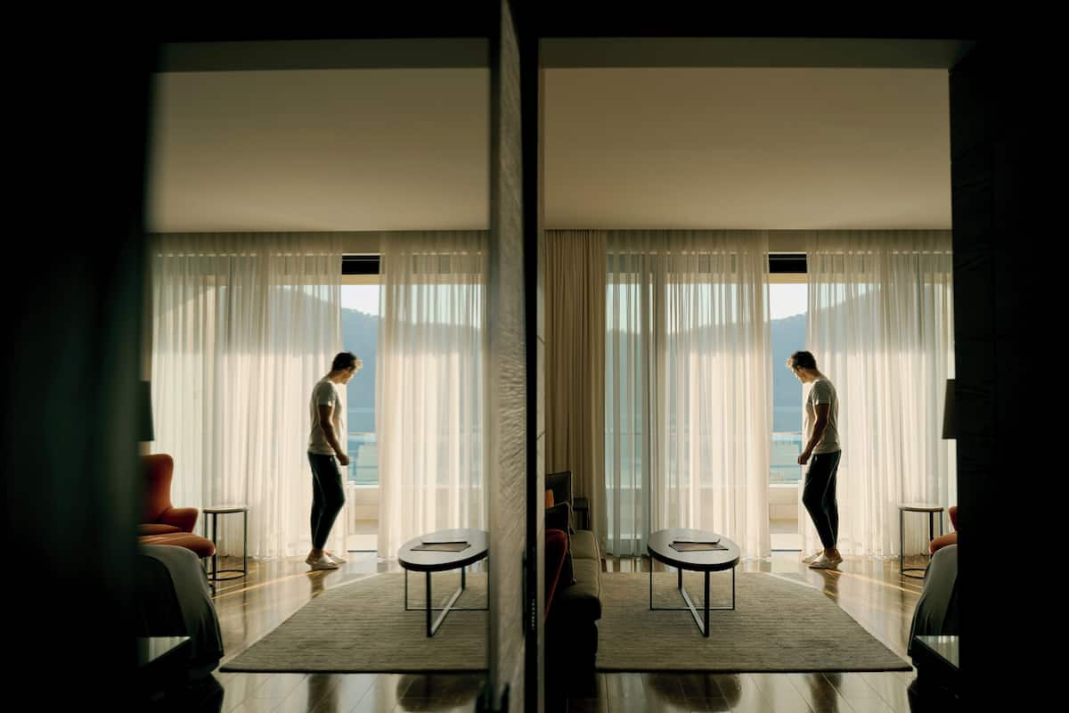 A modern hotel room with a large window, a sofa, a coffee table, and a view of the sea.