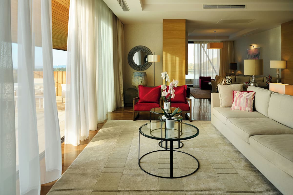 A modern hotel room with a living area, a dining area, and a view of the outdoors.