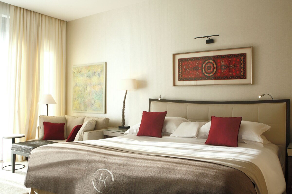 A hotel room with a large bed, a nightstand, a lamp, and two paintings on the wall.