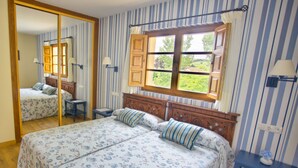 Een slaapkamer met een groot bed, een spiegel, een raam met luiken en gestreept behang.