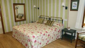 A bedroom with a striped green and white wall, a bed with floral bedding, a nightstand, a chair, a mirror, and a framed picture on the wall.
