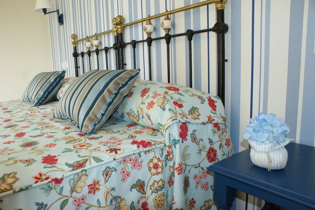 Una cama con ropa de cama floral, almohadas a rayas y una mesita de noche azul con un florero.
