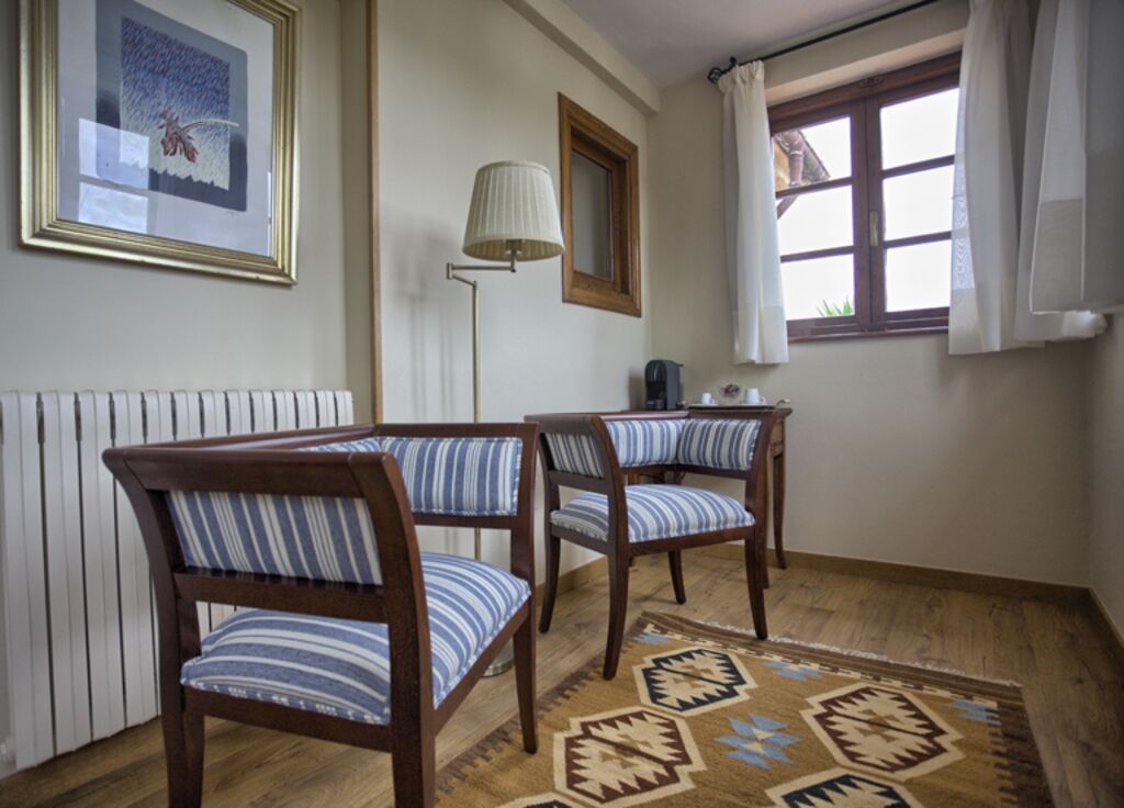 Una stanza con due sedie di legno con cuscini a righe, una lampada da terra, un quadro appeso al muro, una finestra con tende e un tappeto decorato.