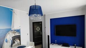 A modern room with a dining area, a black door, a blue accent wall, and a mounted TV. - Family Homes - Apartamenty Rzemieślnicza (Władysławowo)
