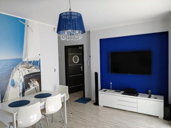 A modern room with a dining area, a black door, a blue accent wall, and a mounted TV.