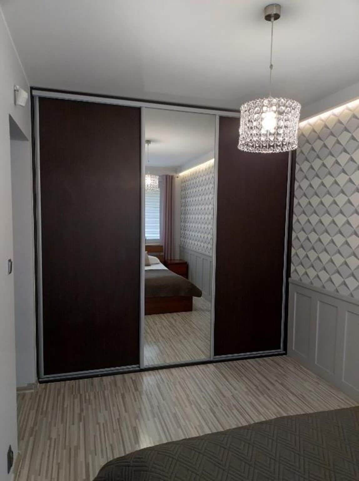 Une chambre dotée d’un grand placard avec porte coulissante, d’un lit recouvert d’une couvre-lit à motifs et d’un lustre.
