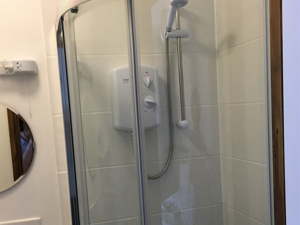 Une douche fermée par des parois en verre, dotée d’un pommeau de douche à main et d’un panneau de commande.