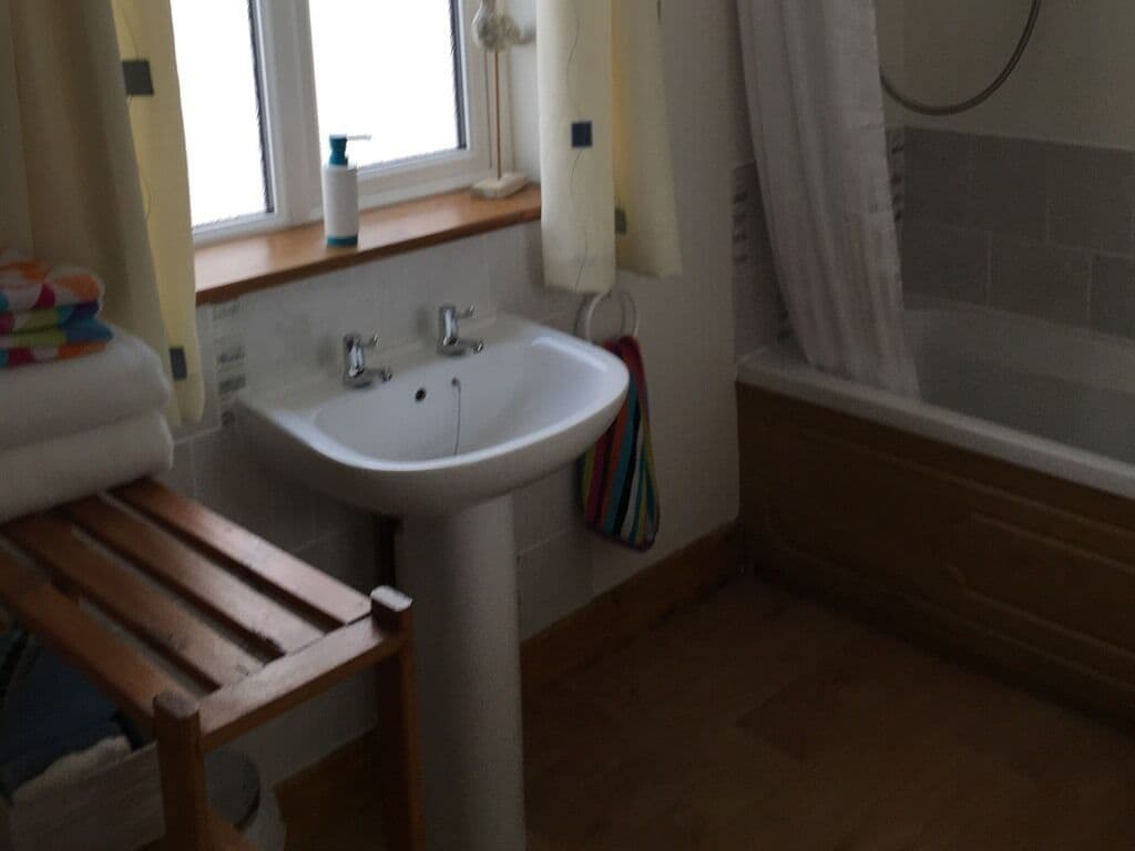 Een badkamer met een wastafel, een houten bankje, een bad en een raam met gordijnen.