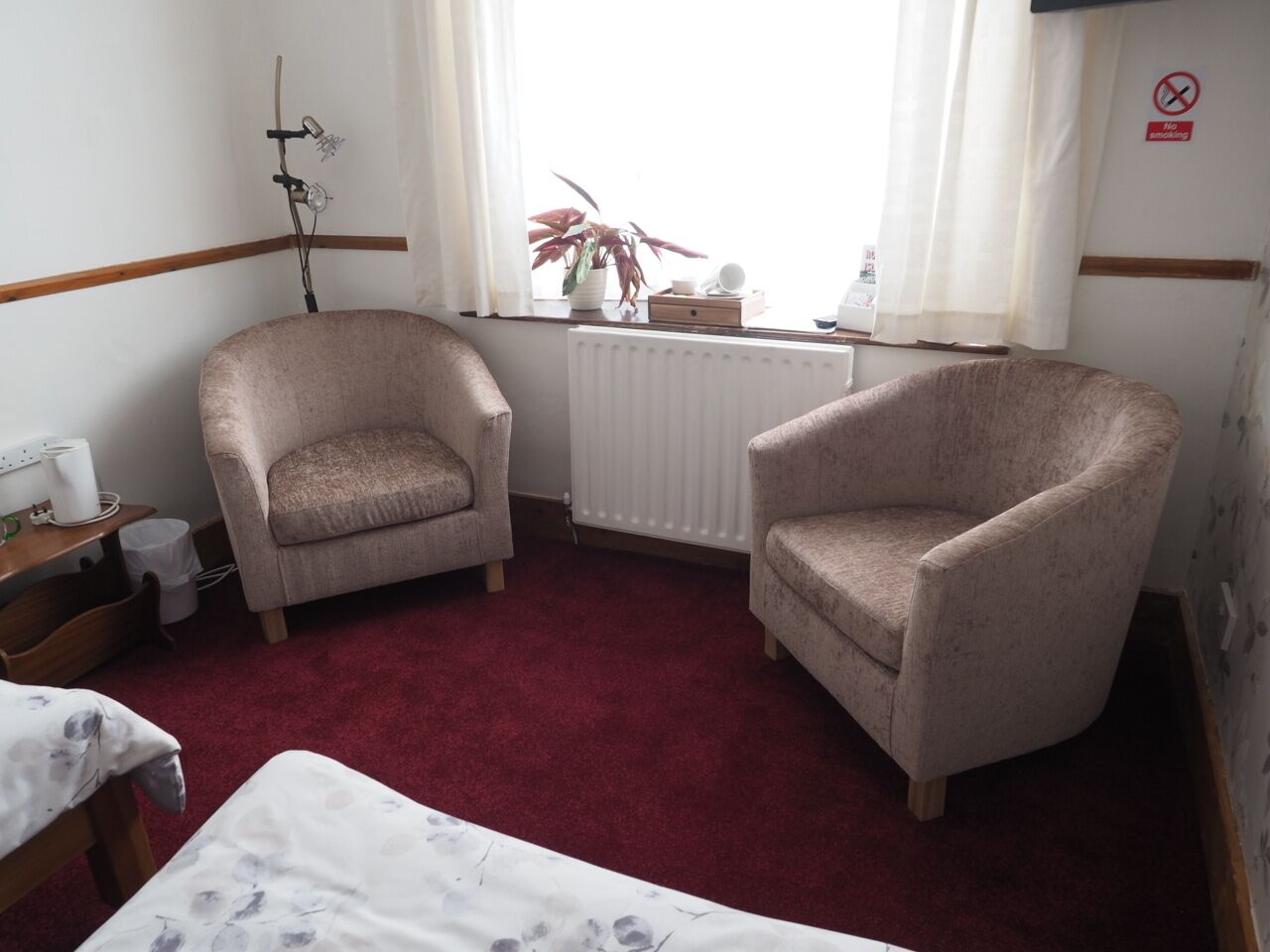 Una habitación con dos sillones, un radiador, una ventana con cortinas, una planta y un cartel de 'No Smoking'.