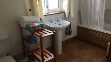 A bathroom with a wooden shelf holding towels and a basket, a white sink, and a window with curtains.