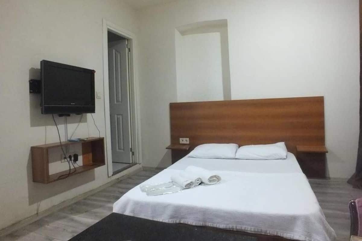 A hotel room with a bed, a television mounted on the wall, and a wooden headboard.