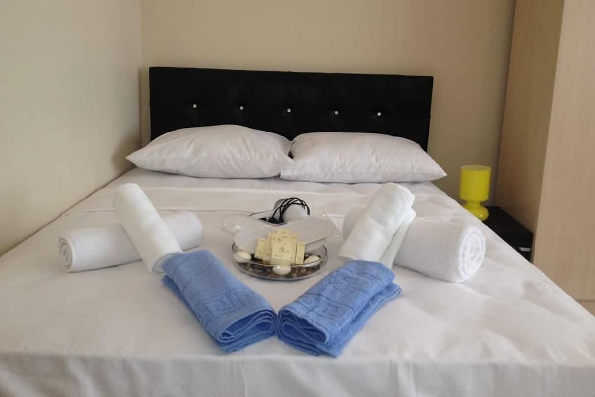 A neatly made bed with white linens, two rolled towels, a tray with toiletries, and a yellow nightstand.